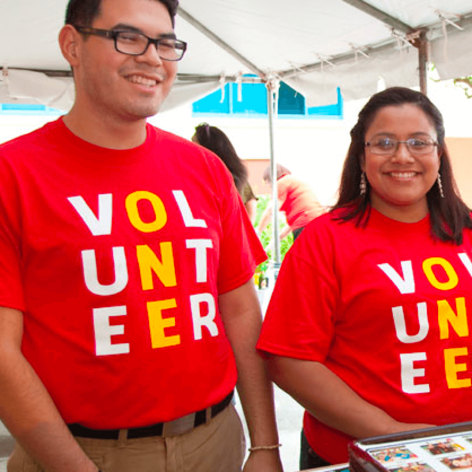 Volunteers fundraising for Ronald McDonald House outdoors under a tent at a public event.